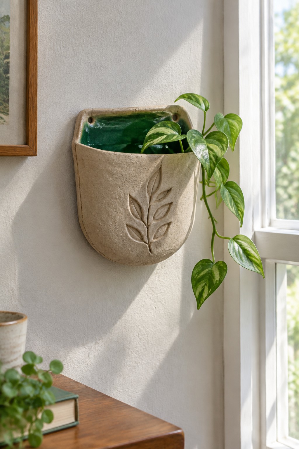 Ceramic wall planter with green glaze and trailing variegated houseplant near window