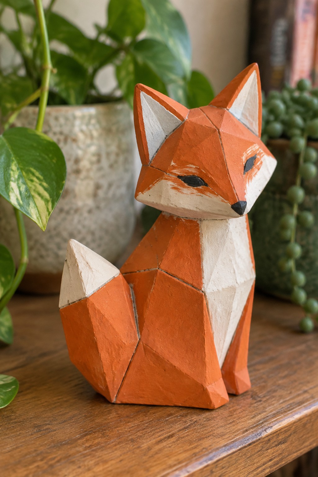 Orange geometric wooden fox figurine on table amid potted green plants