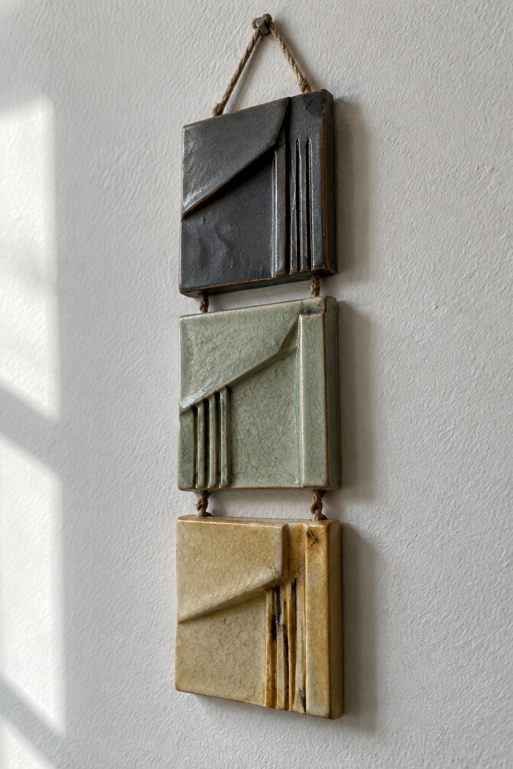 Three hanging ceramic tiles with geometric designs in black, green, and beige tones.