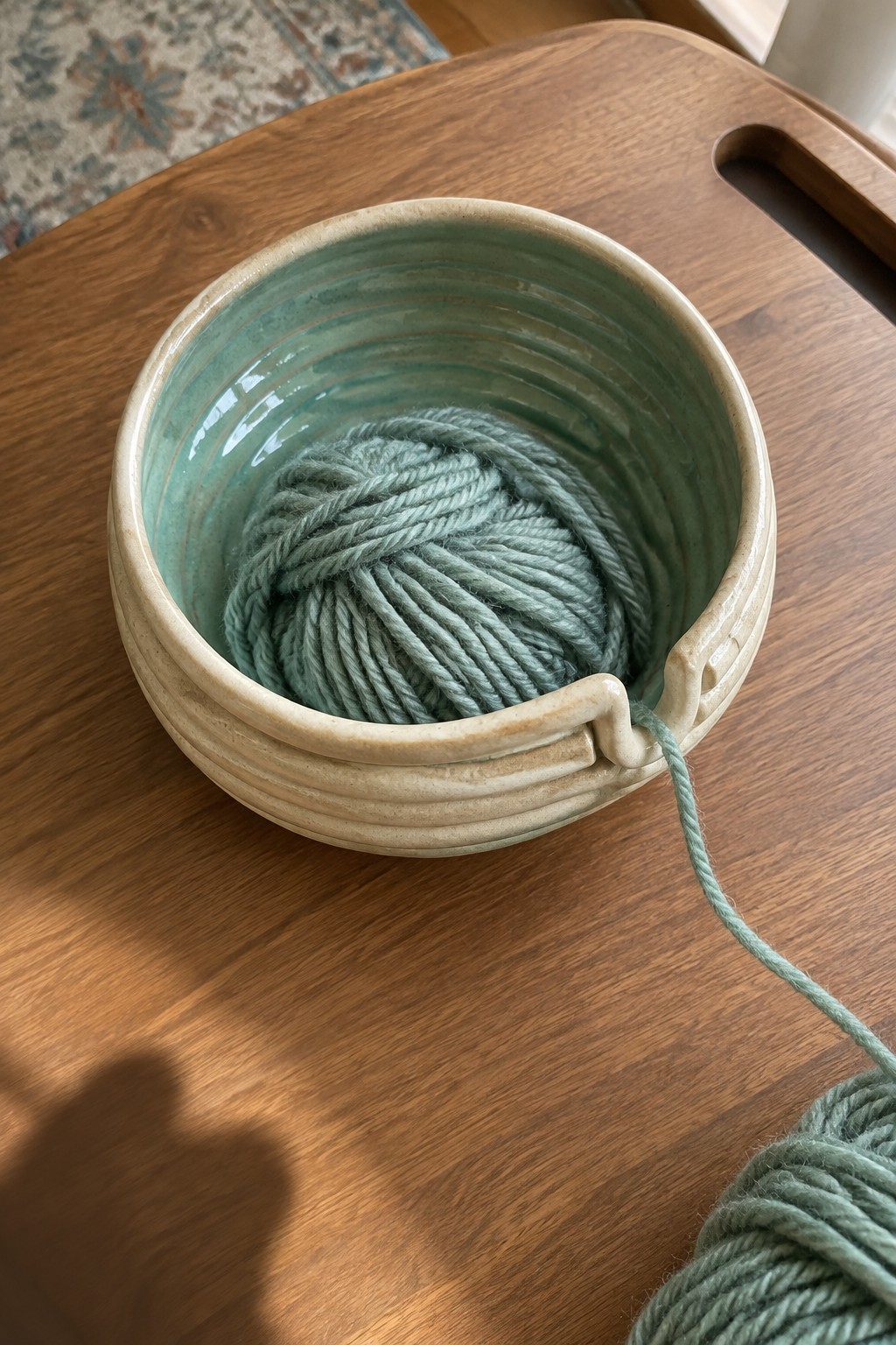 Sage green yarn ball in ribbed ceramic bowl on wooden table