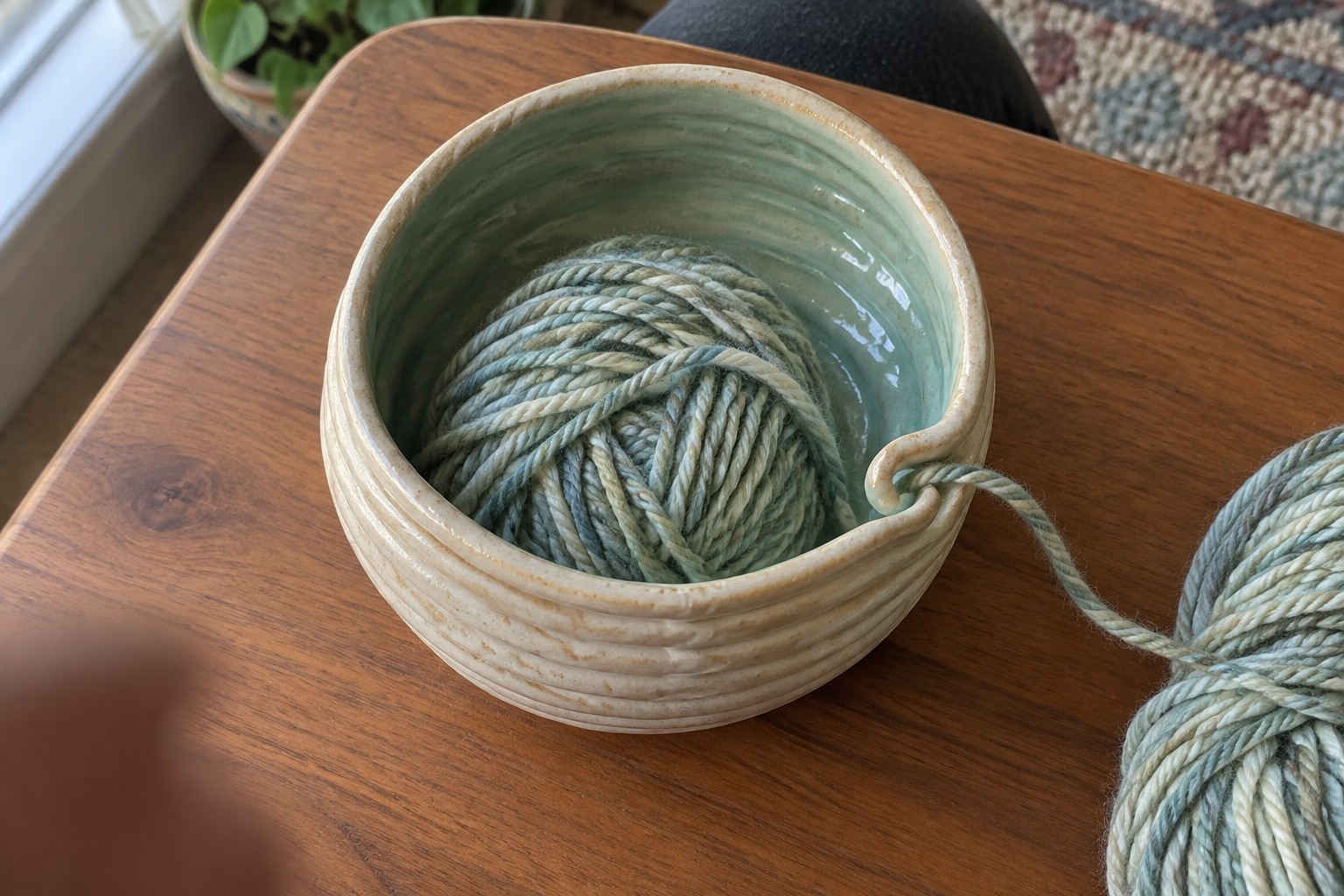 Sage green yarn ball in ribbed ceramic bowl on wooden table