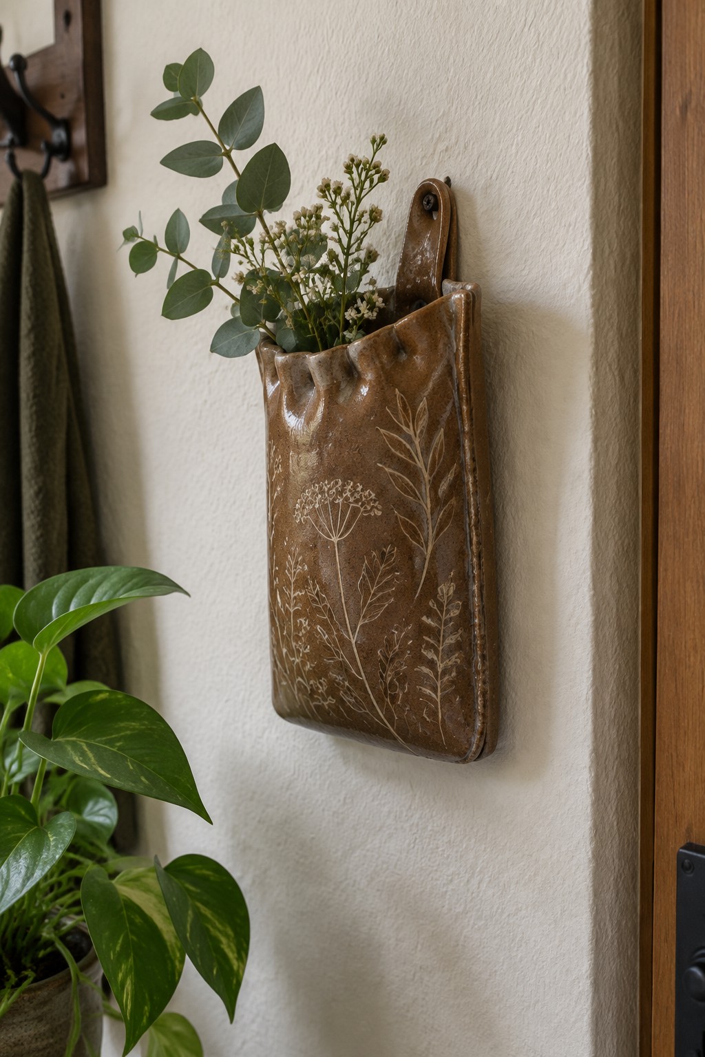 Brown ceramic wall pocket with botanical etchings holding eucalyptus and dried flowers