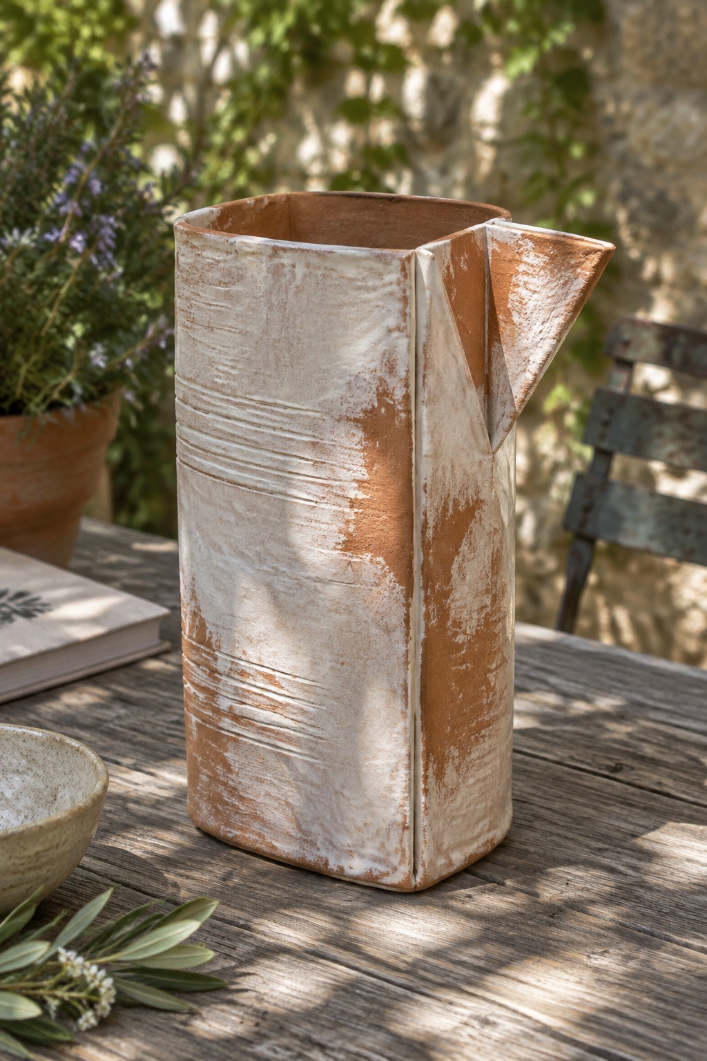 Rustic terracotta and white ceramic pitcher on weathered wooden outdoor table