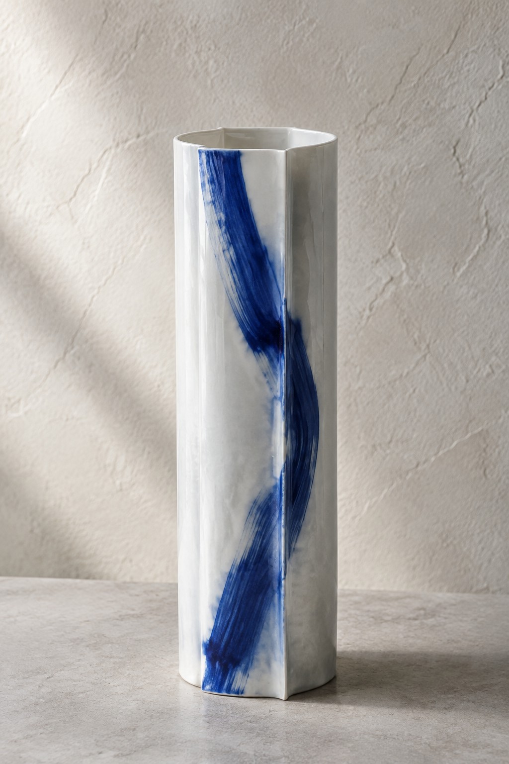 Tall white faceted vase with bold swirling blue brushstrokes on gray surface
