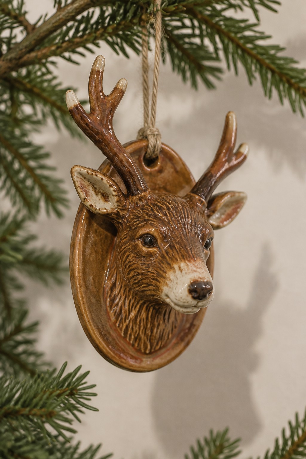 Ceramic brown deer head ornament with antlers hanging from pine tree by twine