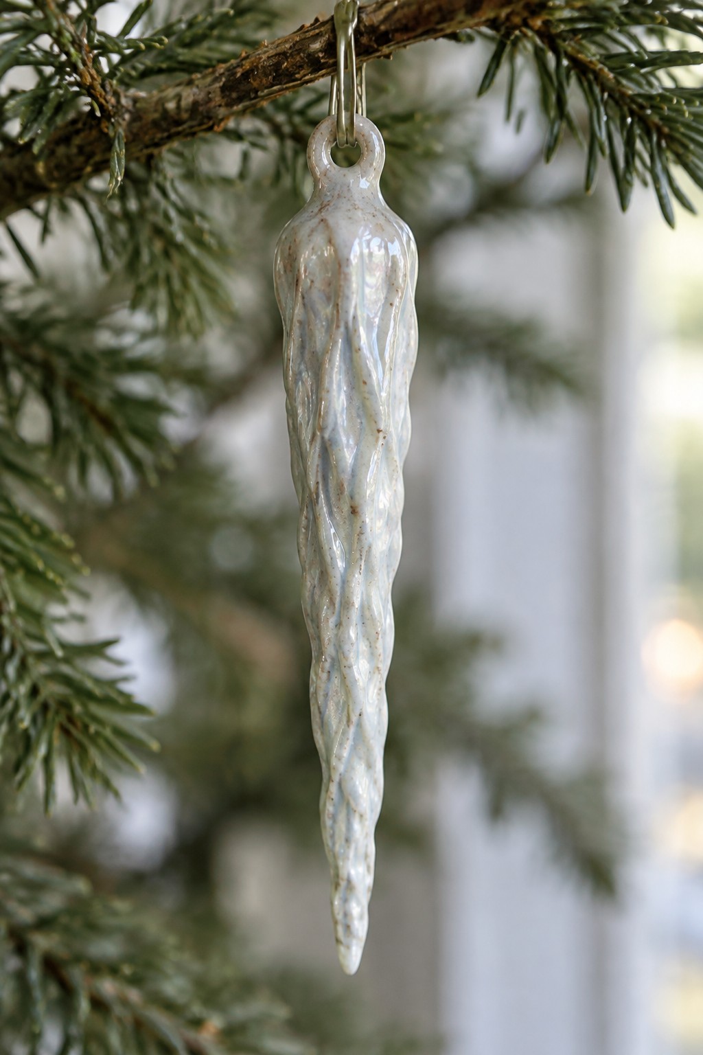 Textured white ceramic icicle ornament hanging from pine tree branch