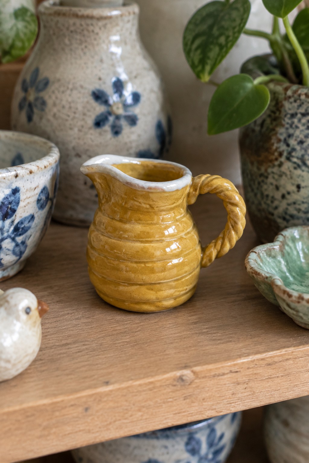 Yellow ribbed pitcher with braided handle amid blue floral ceramics on wood shelf