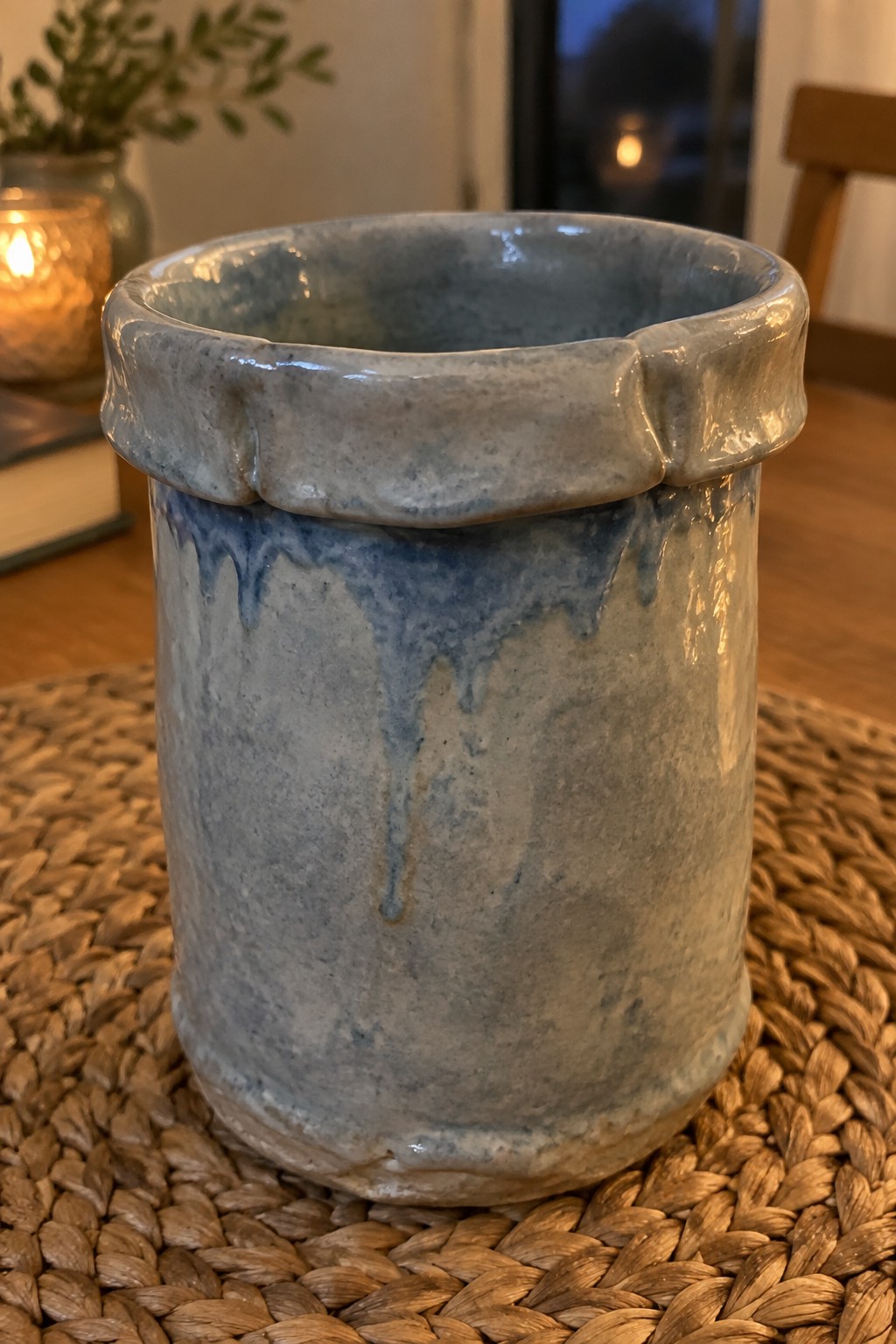 Blue-gray ceramic pot with dripping glaze on woven placemat in warm room