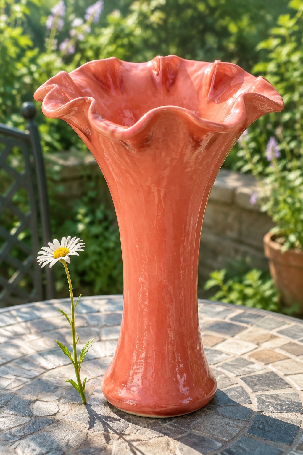 Coral ceramic vase with ruffled rim beside daisy on stone garden table
