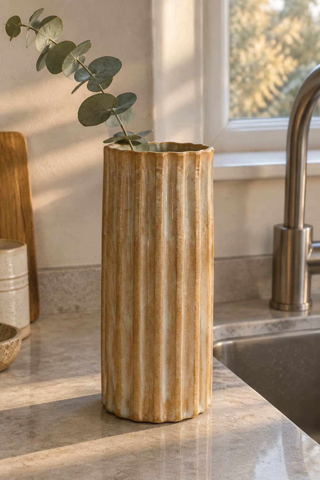 Tall ribbed ceramic vase with eucalyptus on sunlit kitchen marble countertop