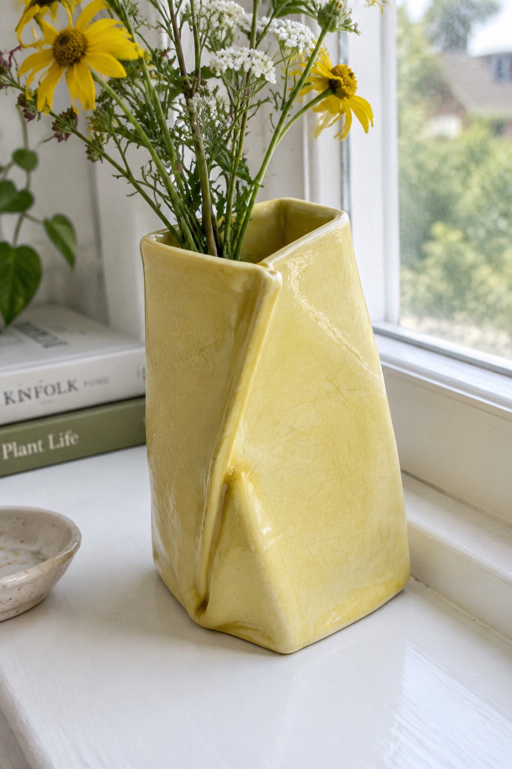 Yellow cracked-glaze vase with yellow and white wildflowers on windowsill