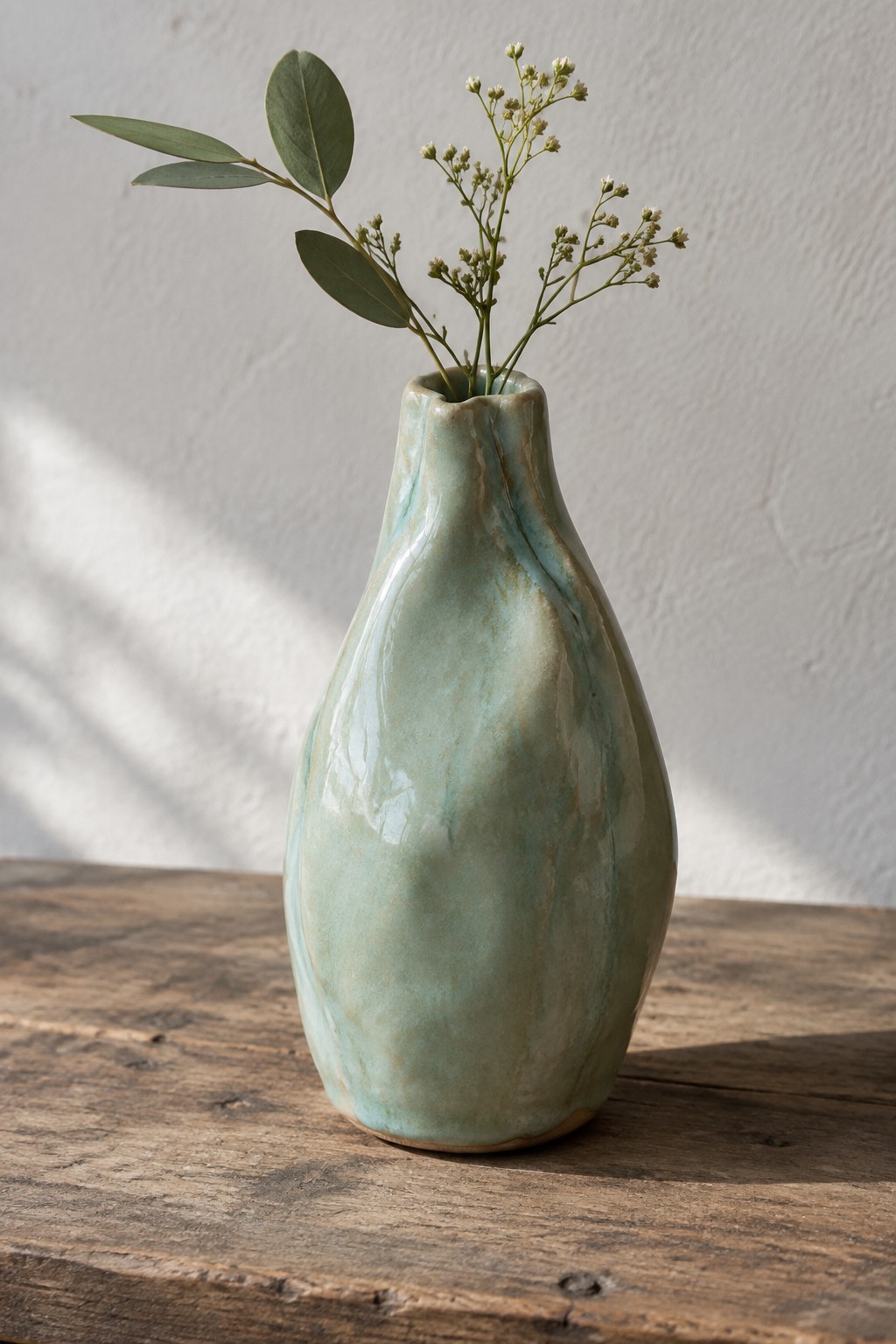 Organic turquoise ceramic vase with green leaves and white flowers on wood table