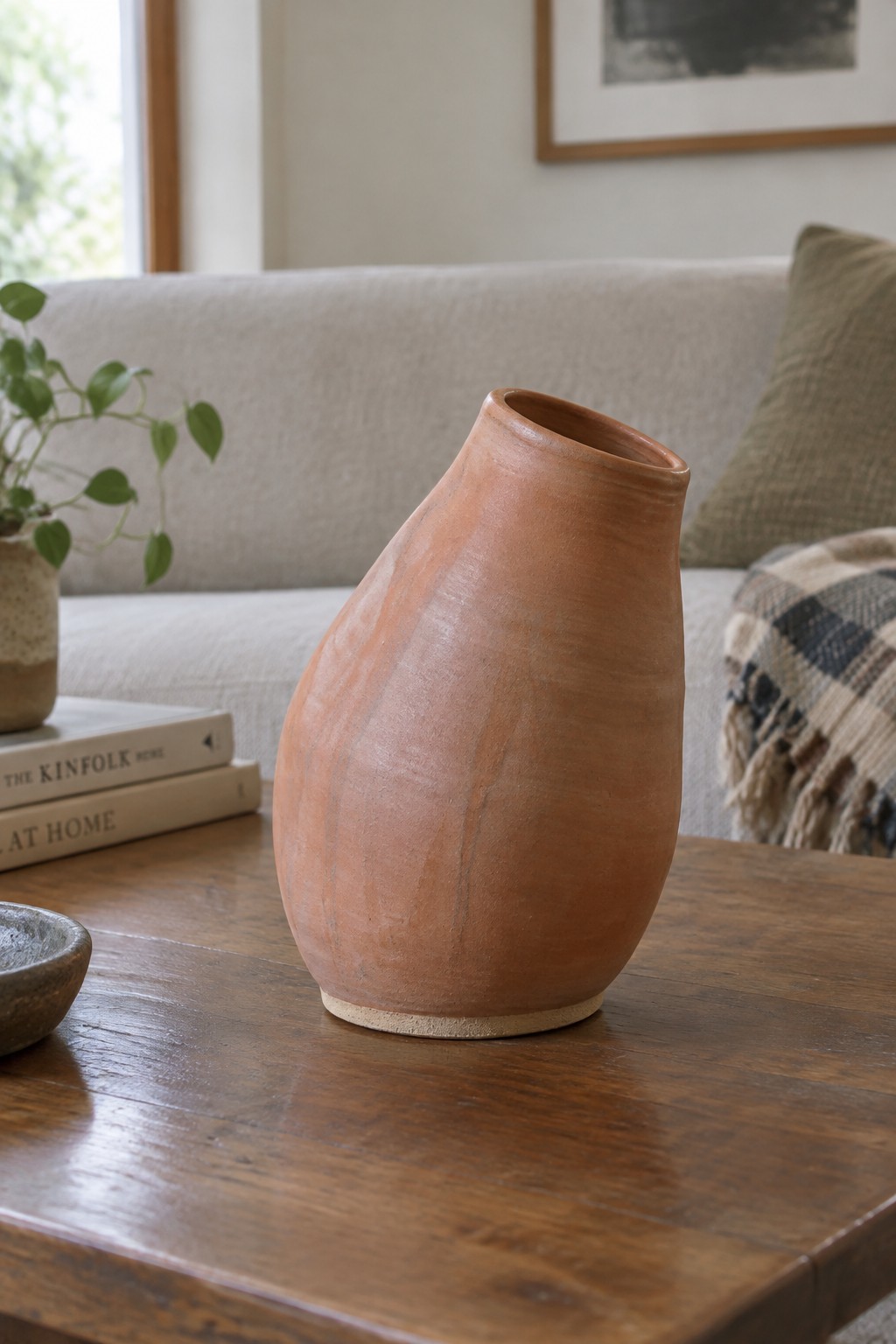 Terracotta vase on wooden table in front of beige sofa with books