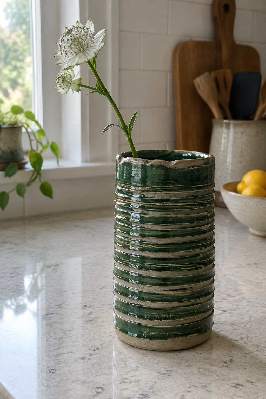 Green ribbed ceramic vase with white flower on marble kitchen counter