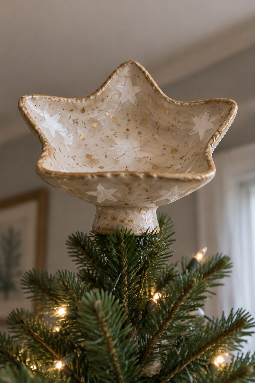 Star-shaped ceramic bowl with white stars and gold speckles atop a lit Christmas tree.