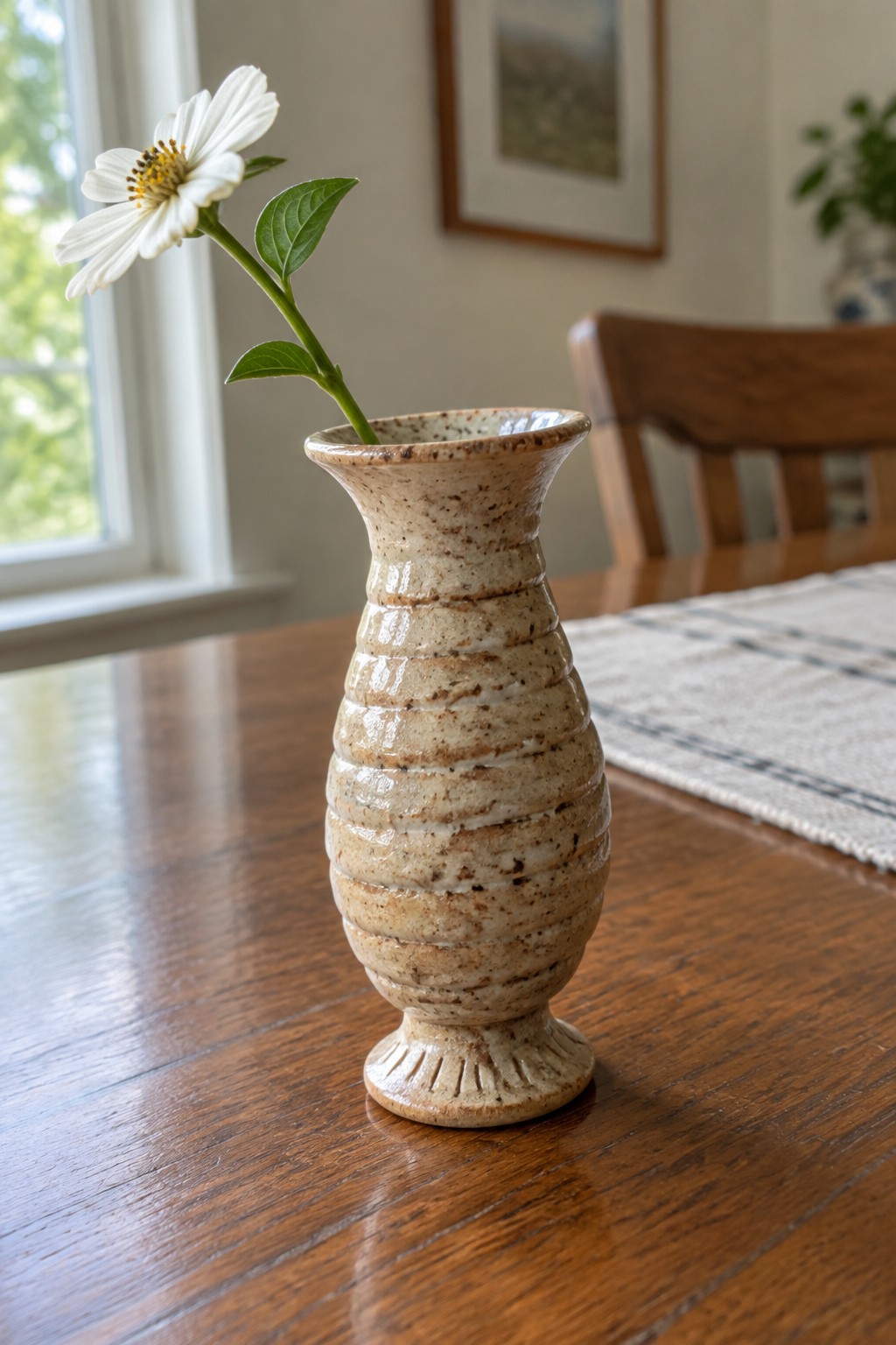 Speckled beige ceramic vase holding white flower on wooden table