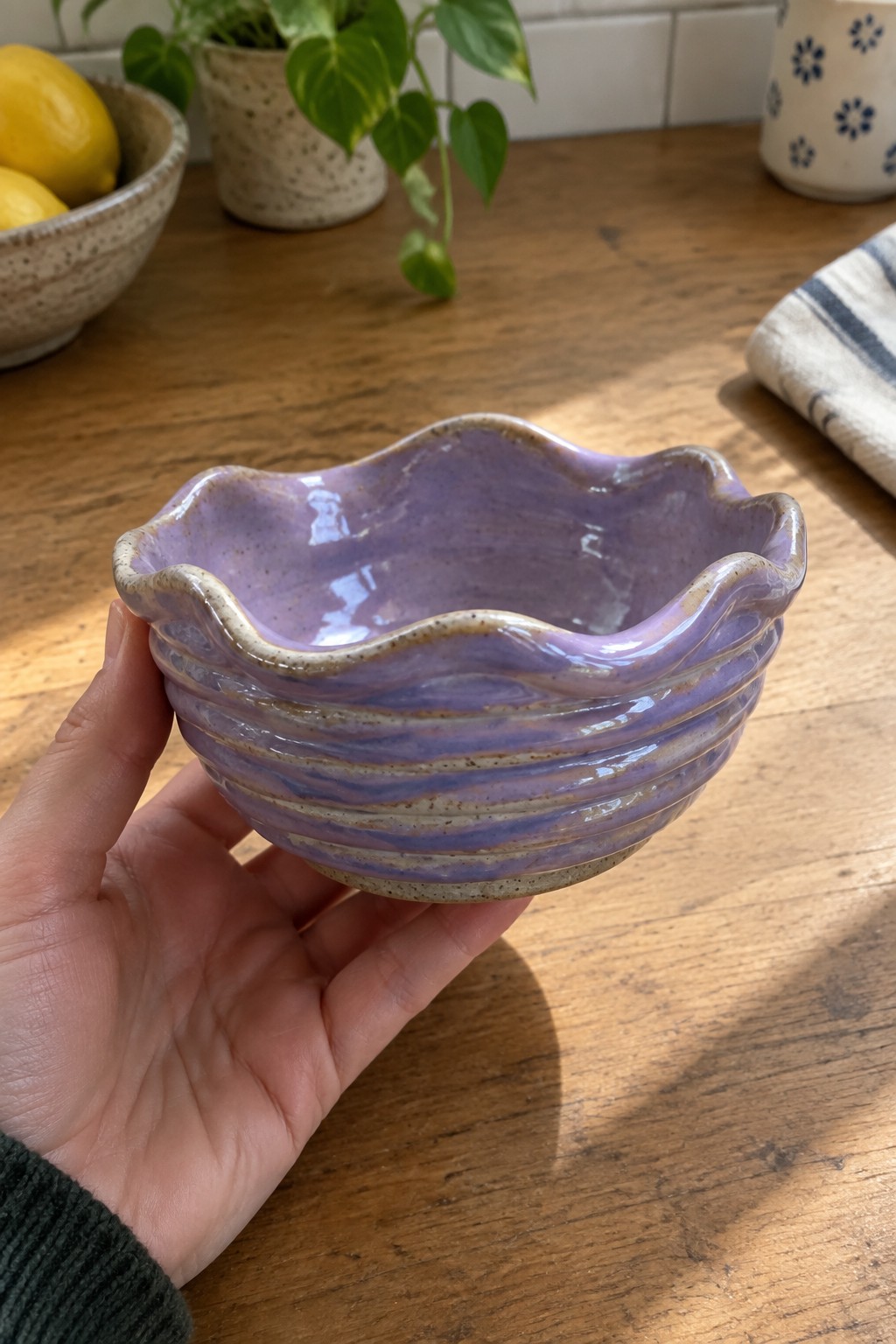 Hand holding ribbed lavender ceramic bowl with wavy rim on wooden table