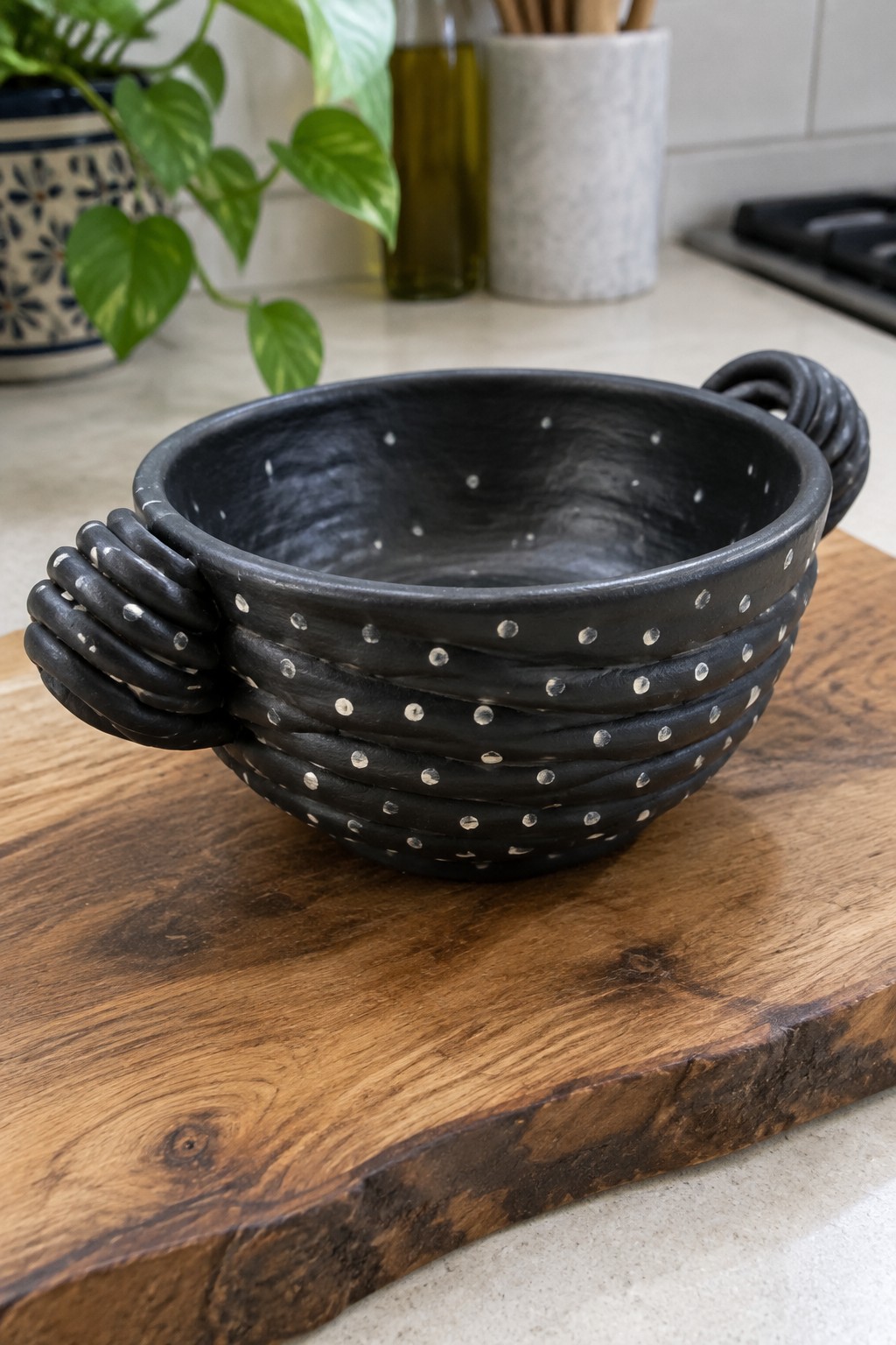 Black ceramic bowl with white dots and twisted handles on wooden board