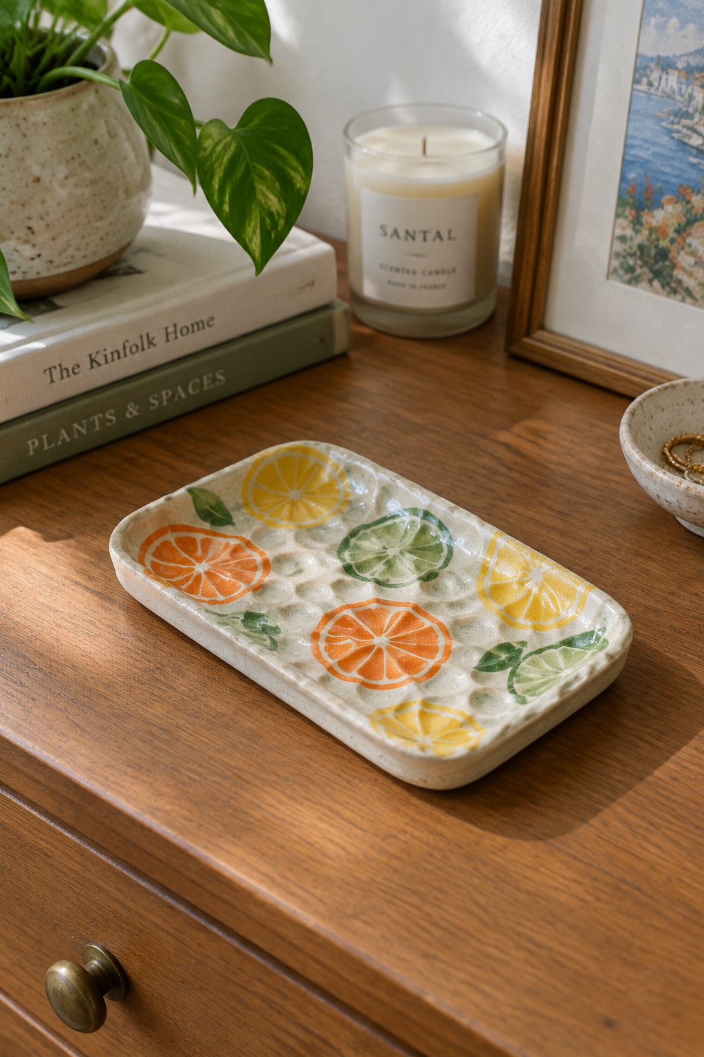 Textured ceramic tray with citrus slices on wooden dresser near candle and books
