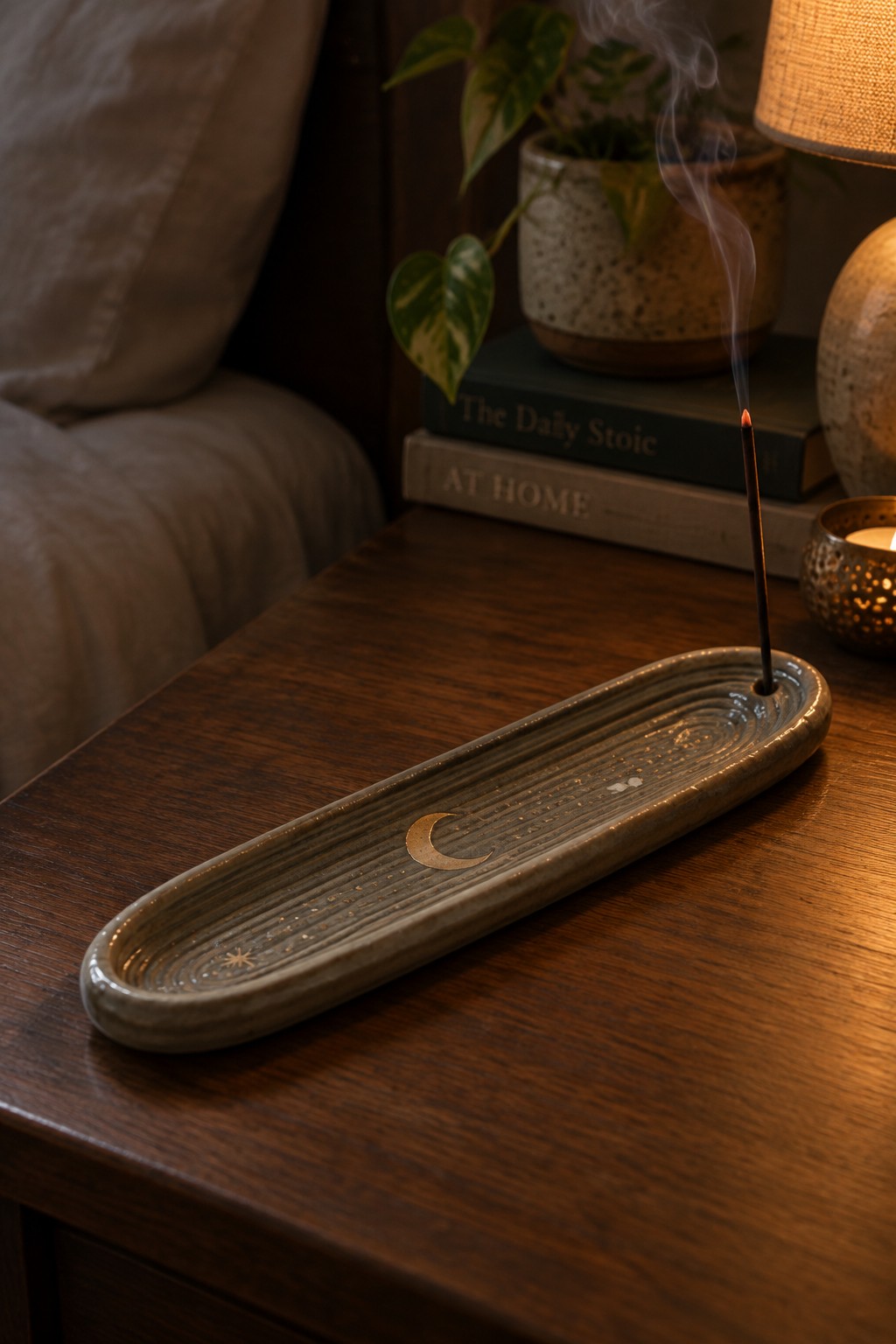 Ceramic incense tray with gold crescent moon, burning stick smoking on wooden table