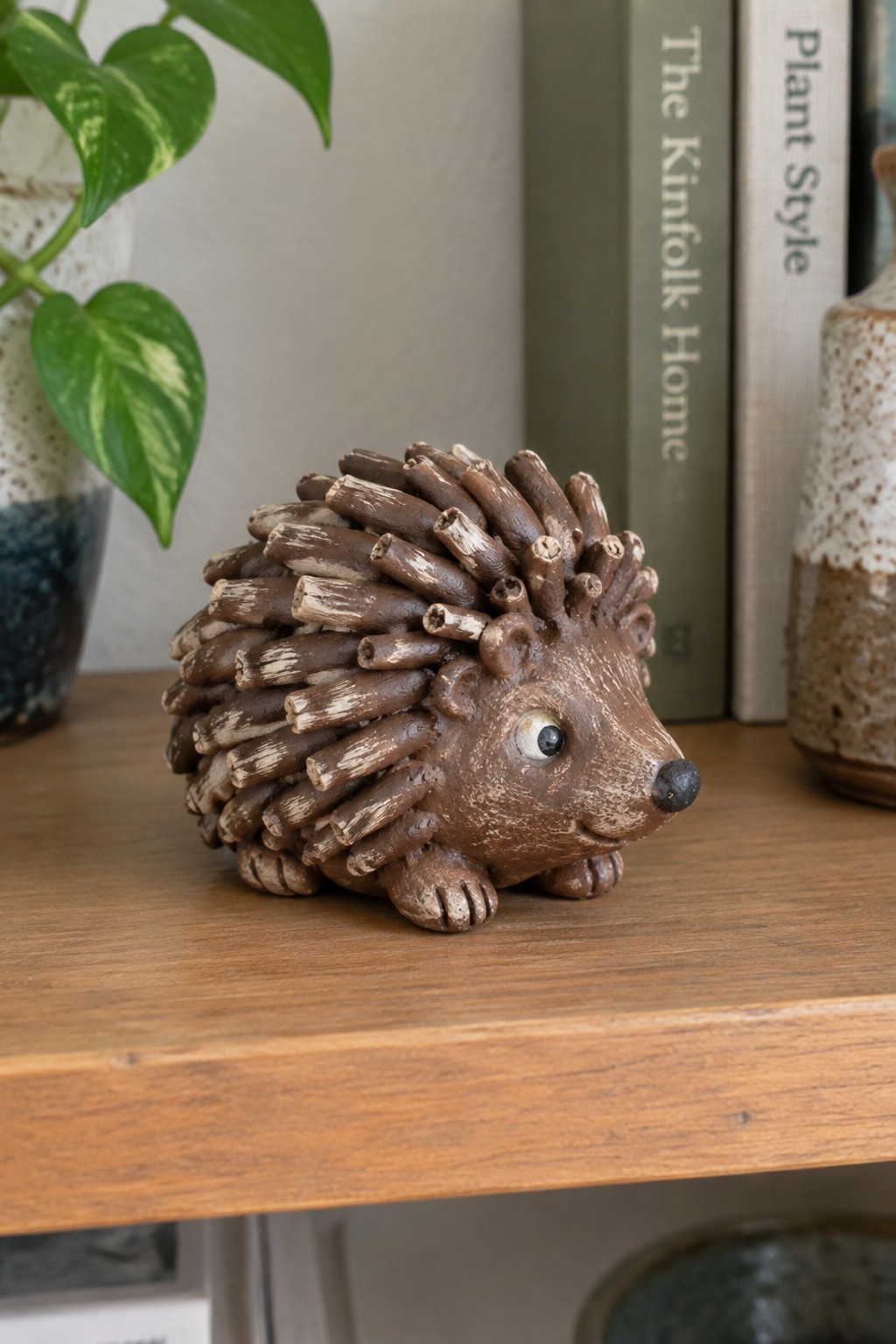 Brown ceramic hedgehog figurine with spiky spines on wooden shelf near books and plant