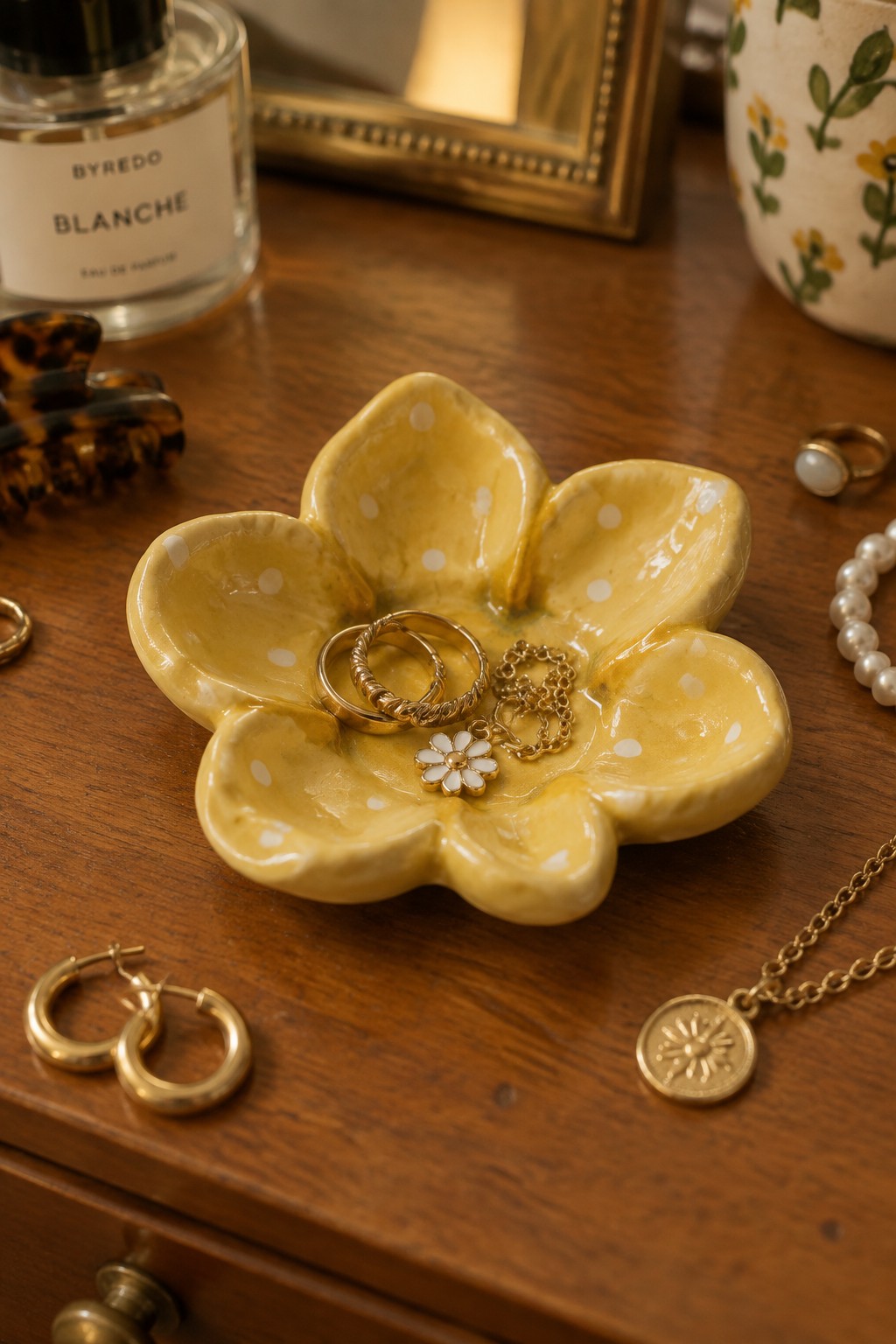 Yellow polka-dotted flower dish holding gold rings and necklaces on wooden vanity