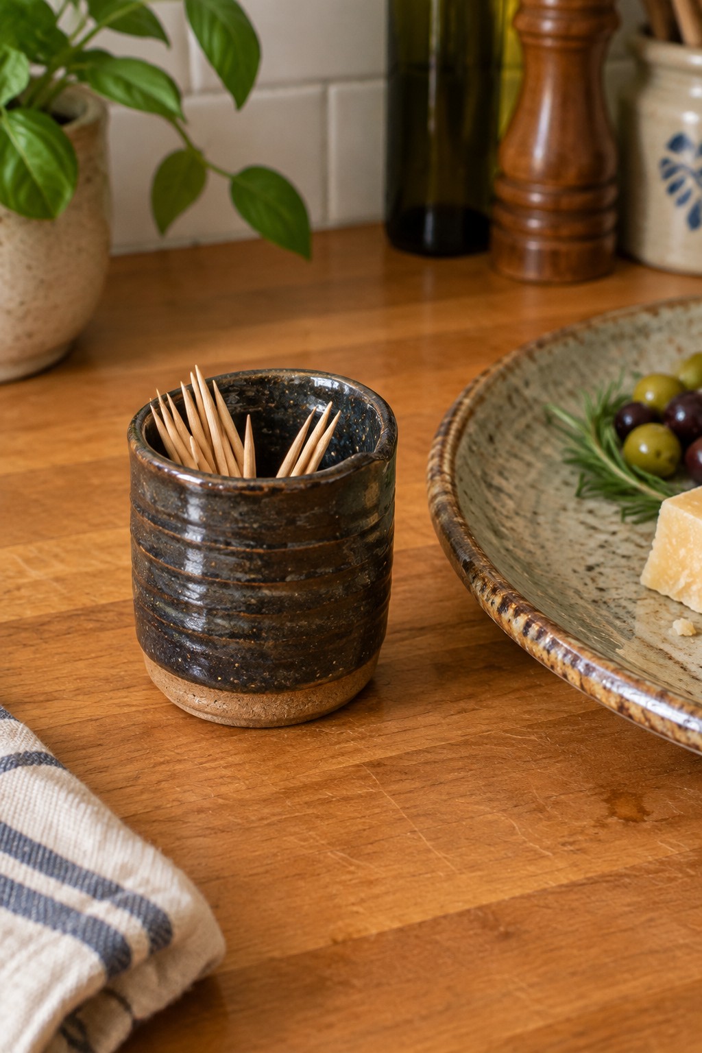 Rustic dark ceramic toothpick holder beside olives and cheese on wooden table