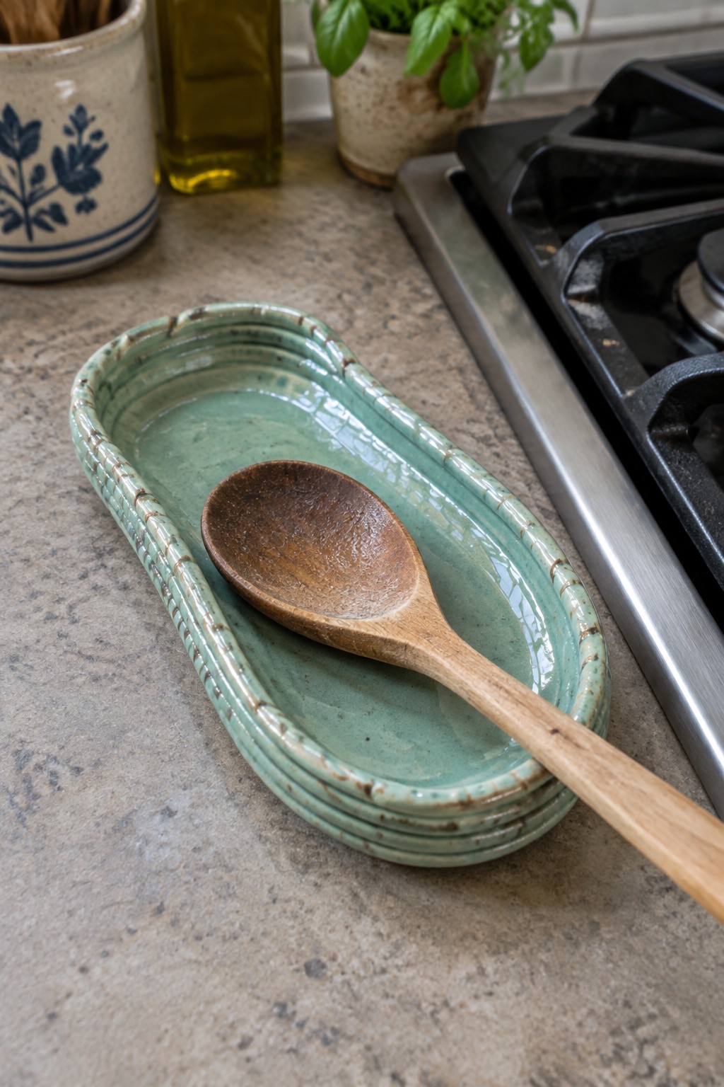 Wooden spoon on stack of green ceramic dishes beside black gas stovetop