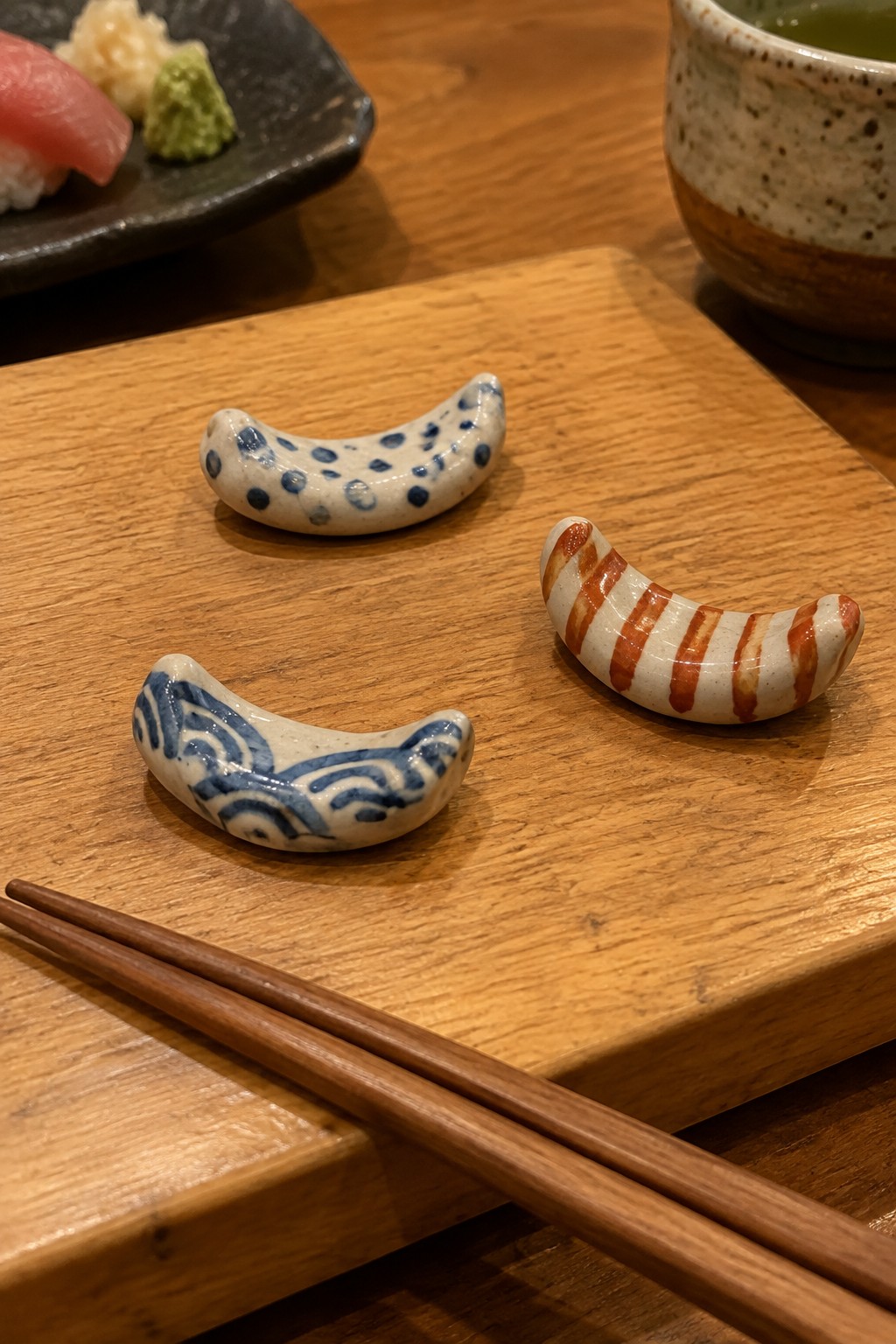 Three patterned ceramic chopstick rests with wooden chopsticks on sushi table.
