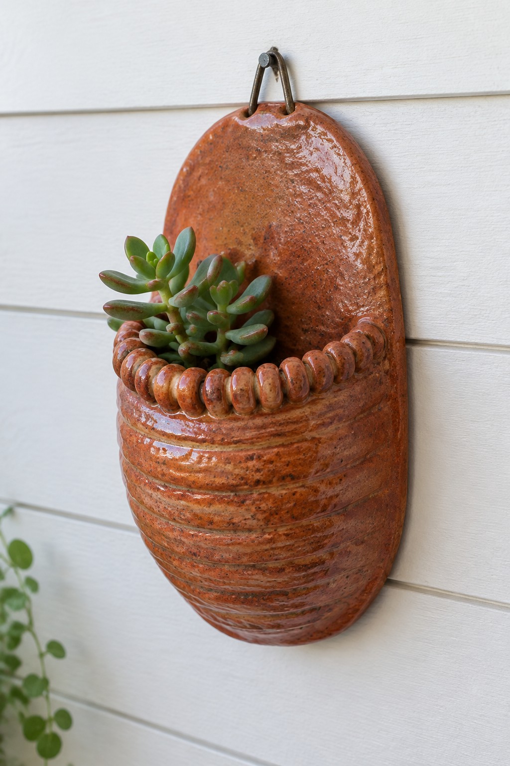 Rustic orange ceramic wall planter with succulent on white siding